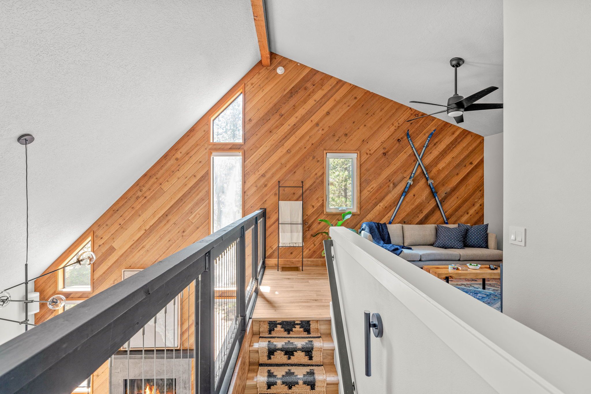 Ein stilvolles Loft-Zimmer mit geneigter Decke, Holzbalken, einer Treppe, einer Couch und einem Deckenventilator.