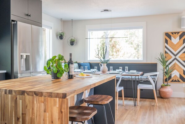 A modern kitchen with a wooden island, bar stools, and a dining area with a view of the outdoors. - Cozy Sunriver Fall Escape+3BR Family Getaway+Sleeps 8+Wood Burning Fireplace (Sunriver)