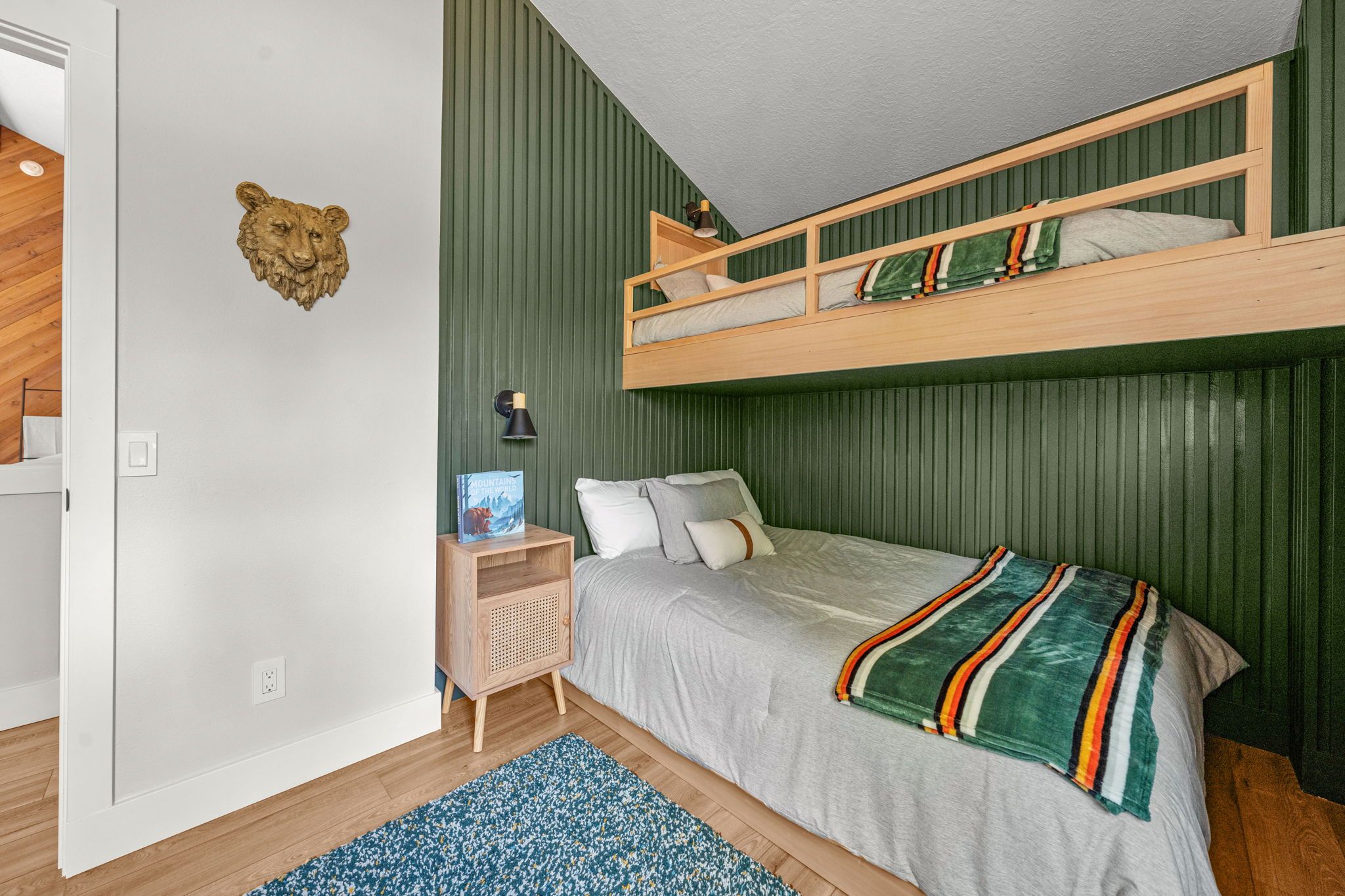 A bunk bed room with a green wall, a nightstand, a lamp, and a book.