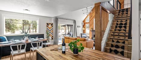 A modern kitchen with a wooden island, dining area, and a staircase with a patterned rug.