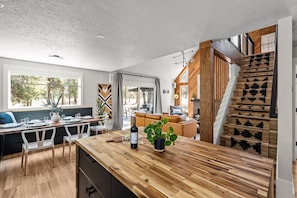 Une cuisine moderne avec un îlot central en bois, un coin repas et un escalier agrémenté d’un tapis à motifs.