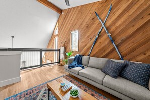 A loft-style room with a sloped ceiling, a grey sofa, a wooden coffee table, and a view of the outdoors. - Cozy Sunriver Fall Escape+3BR Family Getaway+Sleeps 8+Wood Burning Fireplace (Sunriver)