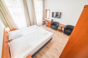 Una habitació d'hotel amb llit, escriptori, cadira, taula petita i televisió penjada a la paret.