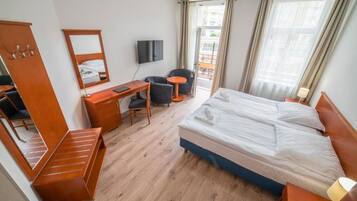 A hotel room with a bed, desk, chair, TV, and a balcony view.