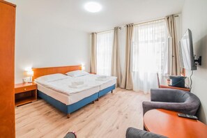 Ein Hotelzimmer mit Bett, Schreibtisch, Sessel, Fernseher und Vorhängen.