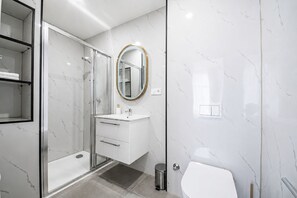 Ein modernes Badezimmer mit Duschkabine aus Glas, einem weißen Waschbecken und einem spiegel mit goldener Umrandung sowie einer Toilette.