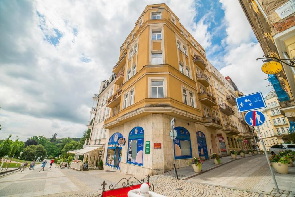 A corner building with multiple floors, a balcony, and a street sign indicating a pedestrian crossing.