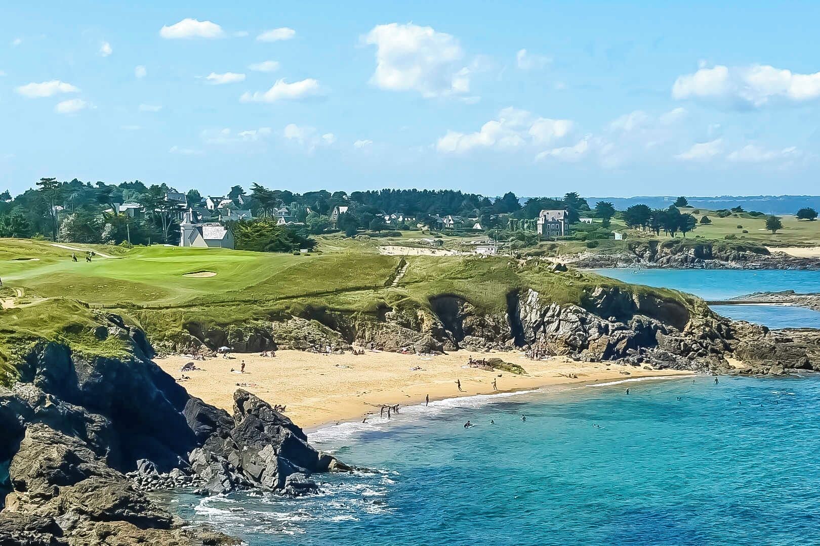A coastal landscape with a beach, rocky shoreline, and a golf course.