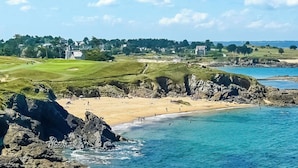 Paesaggio costiero con spiaggia, costa rocciosa e campo da golf.