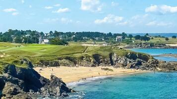A coastal landscape with a beach, rocky shoreline, and a golf course.