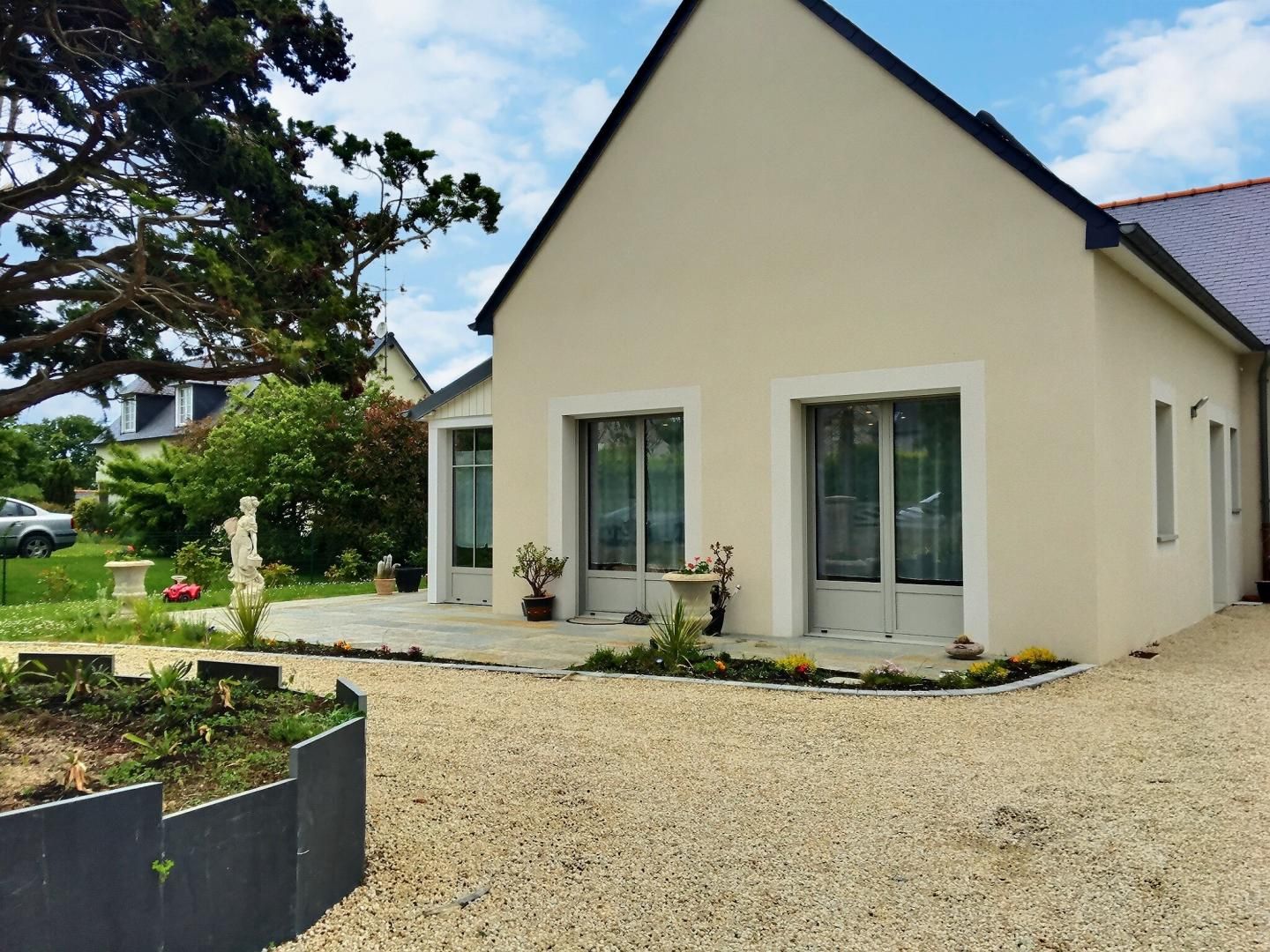 A modern two-story house with a sloped roof, large windows, and a gravel driveway.
