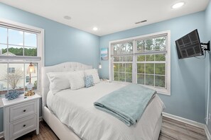 Une chambre avec un grand lit, une table de chevet avec une lampe et une fenêtre donnant sur les arbres.