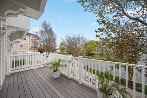 A wooden deck with white railings, potted plants, and a view of a residential street. - Stylish Coastal Townhome | Premier Resort w/ Pools (Berlin)
