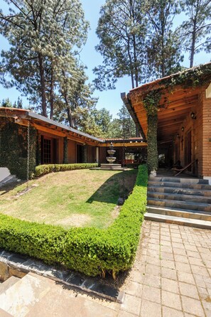 A courtyard with a fountain, surrounded by wooden buildings with stone steps leading up to a covered area. - Heated Indoor Pool, Fire Pit, Billards. (Valle de Bravo)