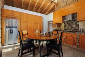 A modern kitchen with wooden cabinets, a stainless steel refrigerator, and a dining area with a round table and chairs. - Heated Indoor Pool, Fire Pit, Billards. (Valle de Bravo)
