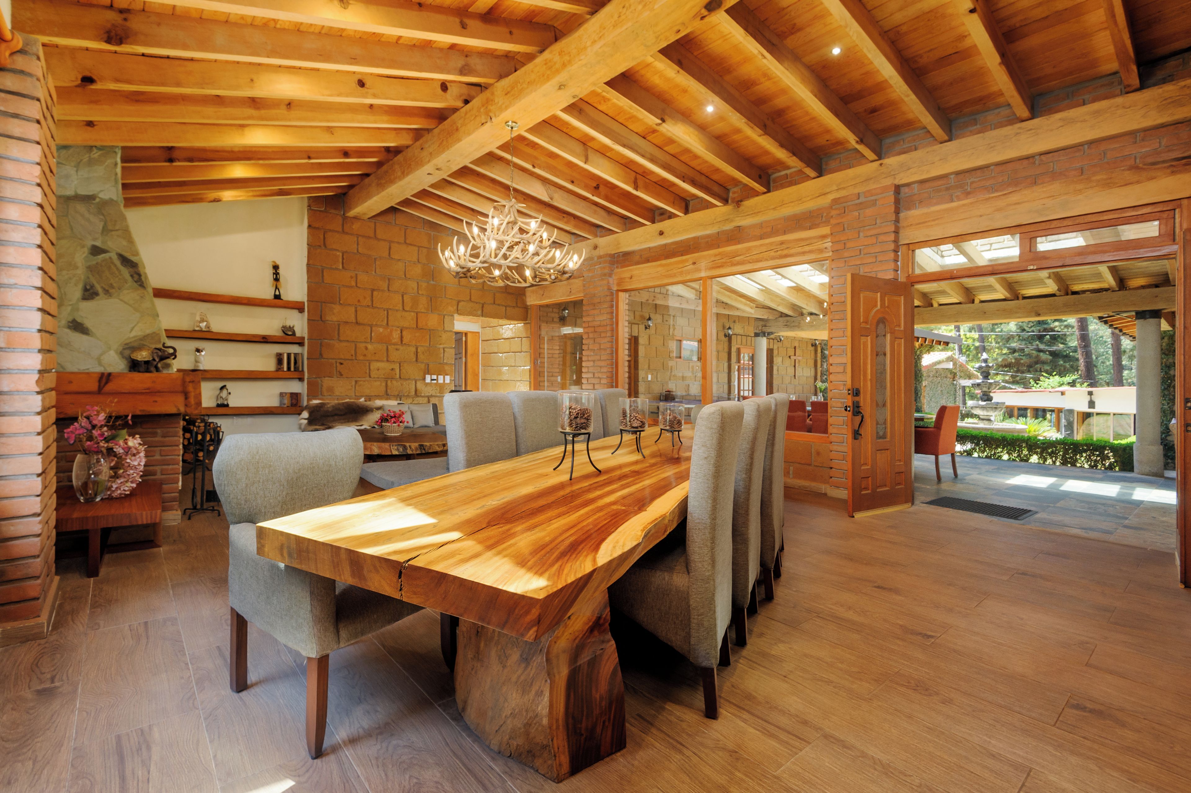 A spacious dining area with a long wooden table and multiple chairs, a chandelier, and a brick wall.