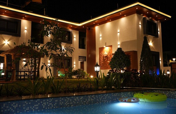 A modern building with a swimming pool, surrounded by plants and a decorative lamp.