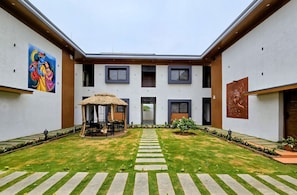 A courtyard with a thatched gazebo, a Buddha relief, and a mural of deities.