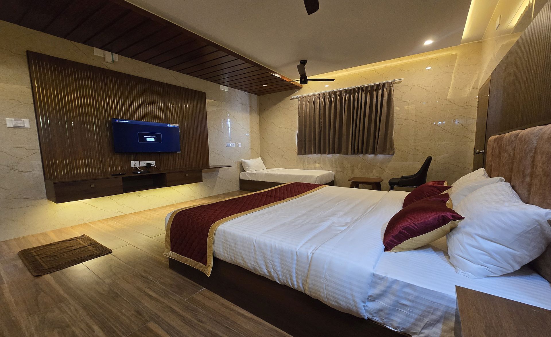 Una habitación de hotel moderna con una cama grande, un televisor montado en la pared, un ventilador de techo y una pared con textura de mármol.