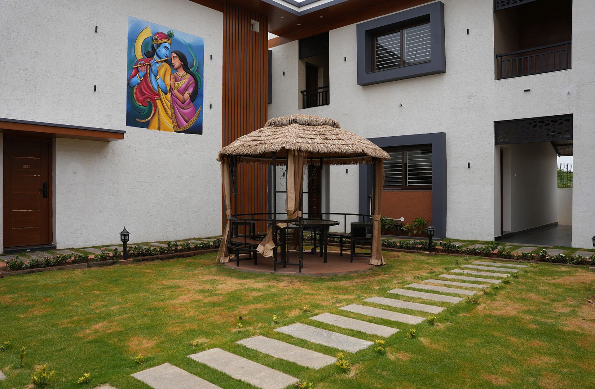 Un edificio moderno con un porche de paja, asientos exteriores y un mural en la pared.