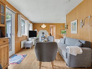 A cozy living room with a sofa, armchair, and a television. There is a fireplace and a window with curtains. - "Karelia" - 900m from the sea by Interhome (Væggerløse)