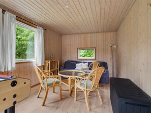 Ein gemütliches Blockhaus-Interieur mit Holzbalkendecke, einer Couch, Korbstühlen, einem Tisch und einem Fenster mit Vorhängen.