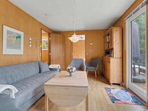Ein gemütliches Zimmer mit einer Couch, einem Tisch mit einer Vase, einem Sessel, einem Schrank und einem großen Fenster.