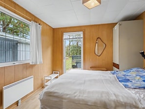 Ein Schlafzimmer mit einem großen Bett, einem Fenster mit Vorhängen, einem Heizkörper und Blick ins Freie.