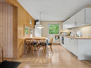 A modern kitchen with wooden flooring, white cabinets, and a dining area with wooden chairs. - "Karelia" - 900m from the sea by Interhome (Væggerløse)
