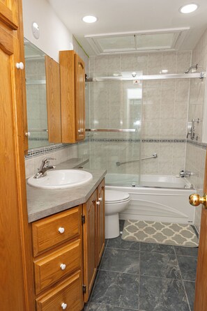 Ein modernes Badezimmer mit einem Holzkosmetikschrank, einem Waschbecken, einer Toilette, einer Duschkabine und einer Badewanne.