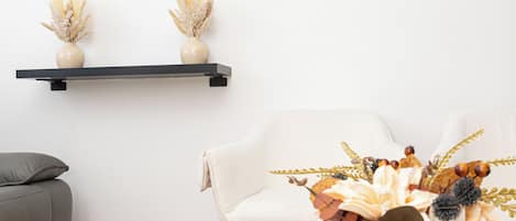 A modern living room with a glass coffee table, a white sofa, and two wall-mounted shelves with decorative items.