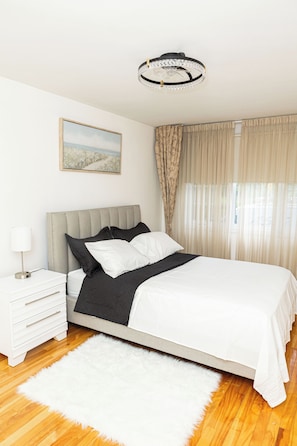 Quarto com cama, mesa de cabeceira, luminária e um quadro na parede.