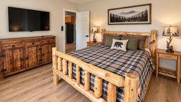 A bedroom with a wooden bed frame, a television mounted on the wall, a wooden dresser, and a painting above the bed.