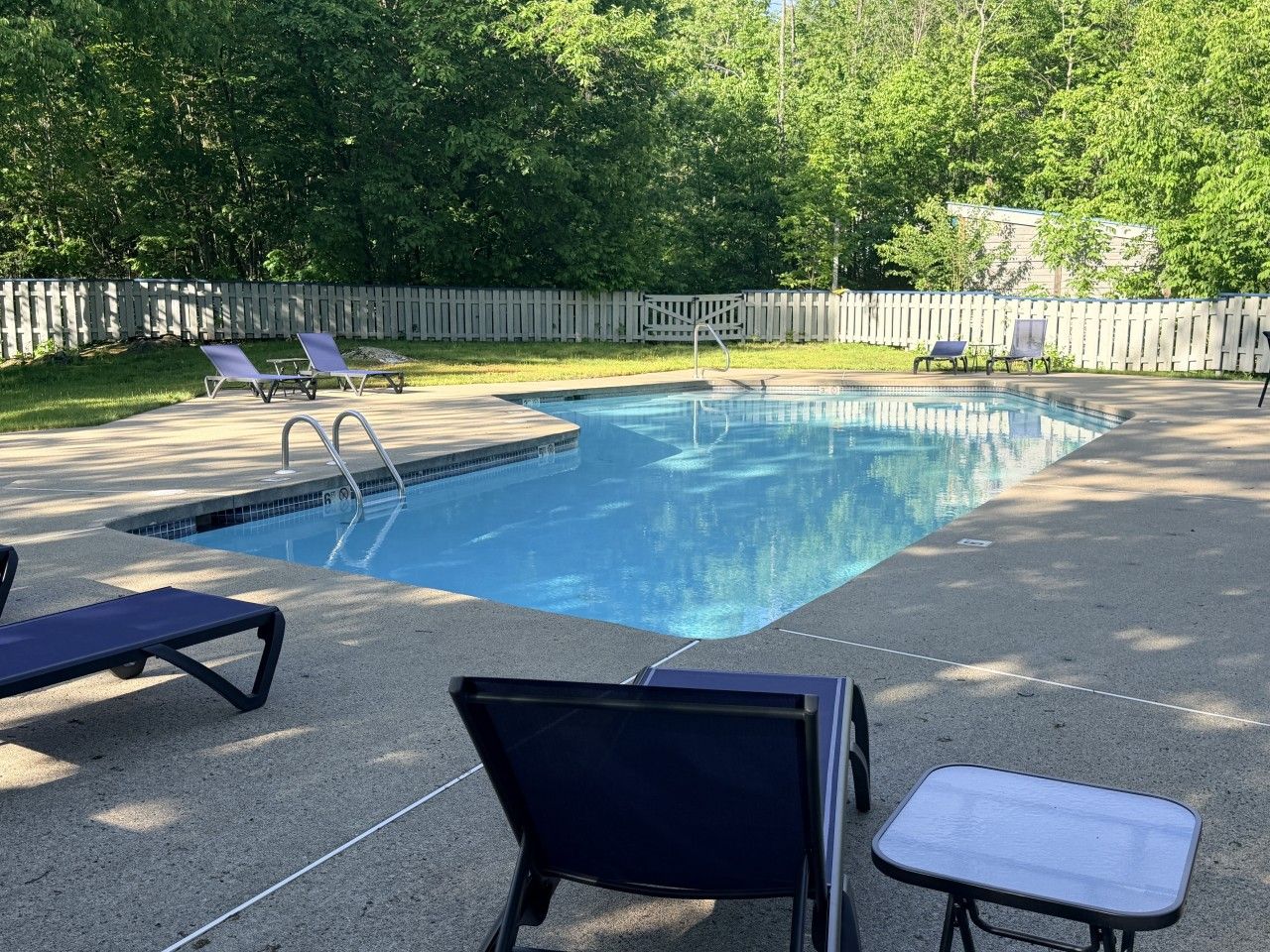 A swimming pool with lounge chairs and a wooden fence in the background.