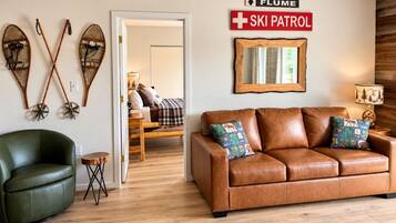 A living room with a leather sofa, a green armchair, and a wooden side table. There is a sign that reads 'FLUME SKI PATROL' on the wall.