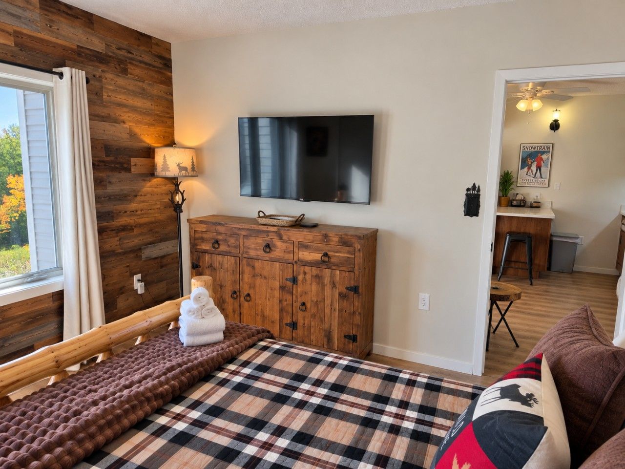 Una habitación acogedora con una cama, un aparador de madera, un televisor y una ventana con cortinas.