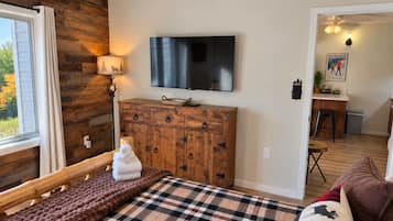 Una habitación acogedora con una cama, un aparador de madera, un televisor y una ventana con cortinas.