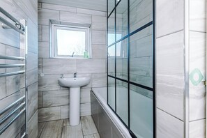 Ein Badezimmer mit einem weißen Waschbecken auf Säule, einem Fenster darüber und einer Duschkabine aus Glas.