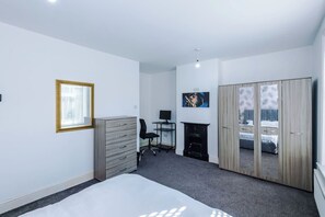 Um quarto com cama, escrivaninha, cadeira, guarda-roupa e lareira.