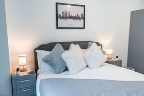 A neatly made bed with fluffy pillows, a framed cityscape picture on the wall, and bedside lamps. - Central 1BR | Private Balcony | Weekday Discount (Greater Manchester)
