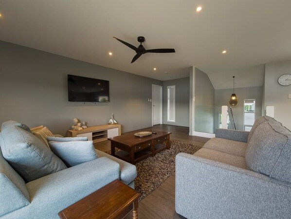 A modern living room with a flat-screen TV, a ceiling fan, and a large window.