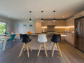 A modern kitchen with wooden cabinets, a stainless steel refrigerator, and three bar stools. - Beachside Bliss - One Bedroom Apartment (Napier)