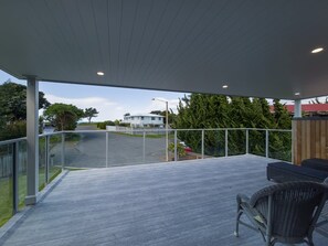 A covered outdoor area with a view of a road and greenery, featuring a seating area with chairs. - Beachside Bliss - One Bedroom Apartment (Napier)