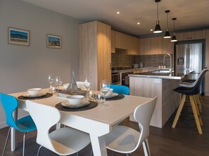 A modern kitchen with wooden cabinets, a built-in island, and a dining area with white chairs and a blue chair.