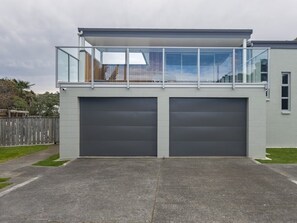 A modern two-story house with a balcony, two garage doors, and a clear sky.