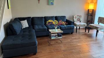 A living room with a sectional sofa, a coffee table with a vase, and a patterned armchair.