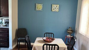 Ein Essbereich mit einem Tisch für vier Personen, umgeben von Stühlen, an einer blauen Wand mit zwei dekorativen Kacheln.