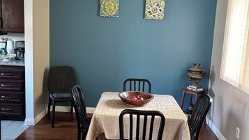 A dining area with a table set for four, surrounded by chairs, against a blue wall with two decorative tiles.