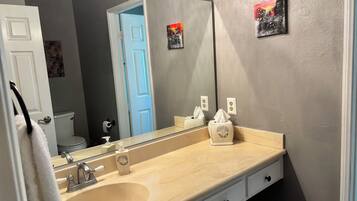 A bathroom with a beige sink, a mirror, a towel rack, and a toilet visible through an open door.