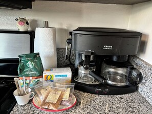 Kahvinkeitin, paketti Starbucks-kahvia, pakkaus Oatly-kaurajuomaa, paketti minttuteetä ja muki, jossa on ruokailuvälineitä, keittiön työtasolla.